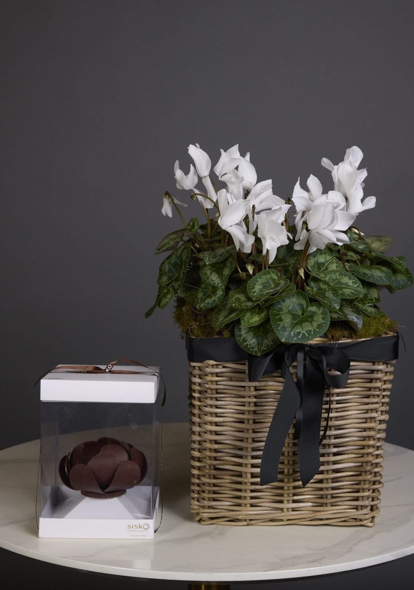 Celebrate beauty in both bloom and bite with the Sweet Bloom gift set – a thoughtful pairing of floral elegance and artisanal indulgence.
Choose from a triple white cyclamen in a woven basket, a double cyclamen in a ceramic vessel, or a single gift-wrapped cyclamen plant. Each option is perfectly paired with a handcrafted chocolate flower by Sisko Chocolate – an exquisite edible creation, meticulously sculpted in Melbourne with passion and precision. A truly unique gift that delights the senses.