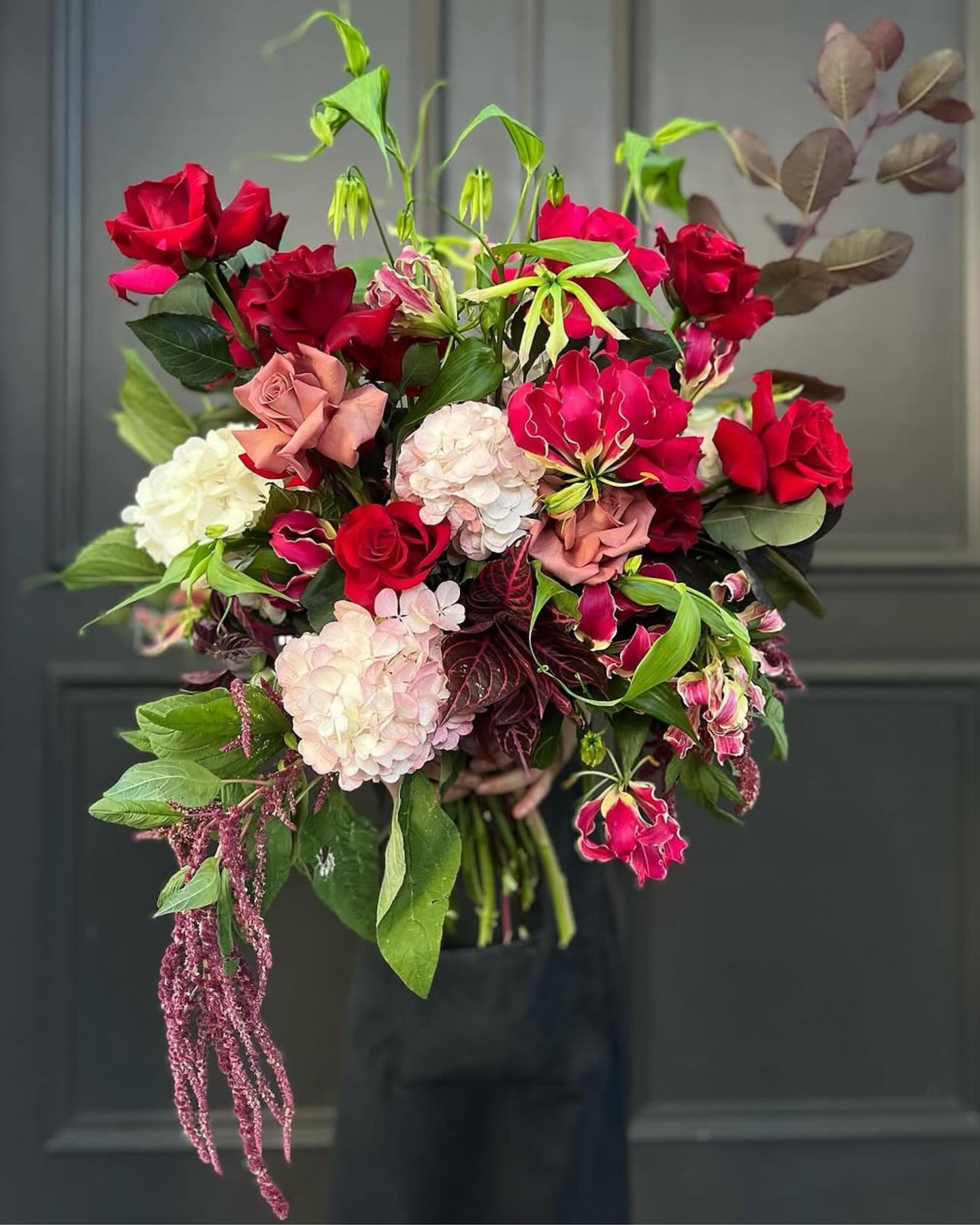 Bouquet of red, pink, and white flowers with green leaves against a dark background