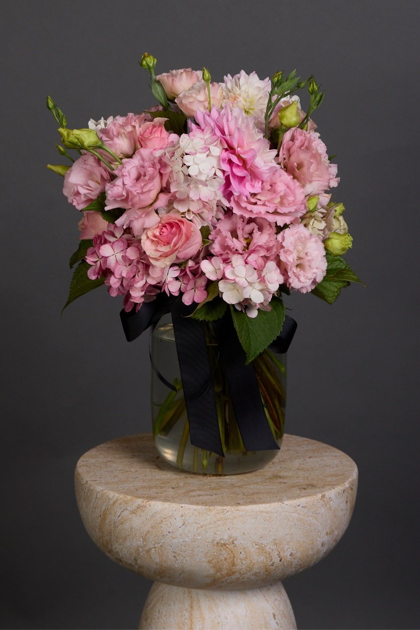A sweet pink selection of seasonal blooms in varying pink hues crafted into a posy-style bouquet with luscious foliage