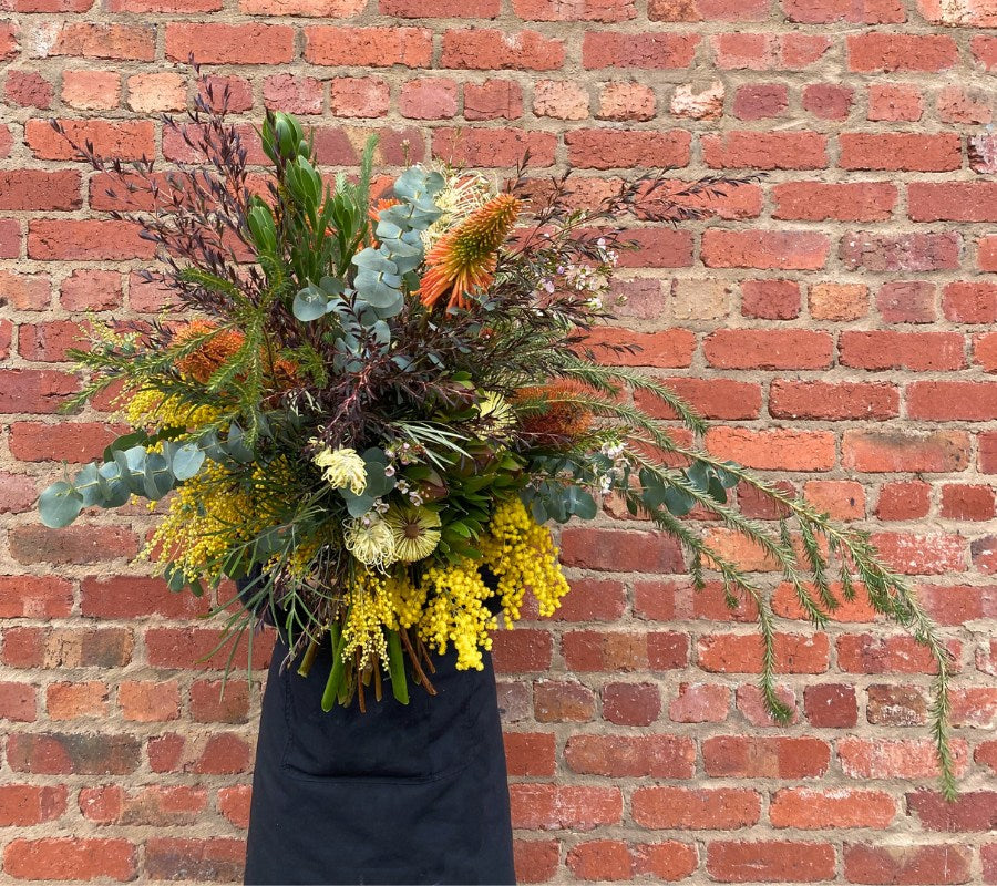 a flower delivery in melbourne of a Floral natives arrangement against a brick wall
