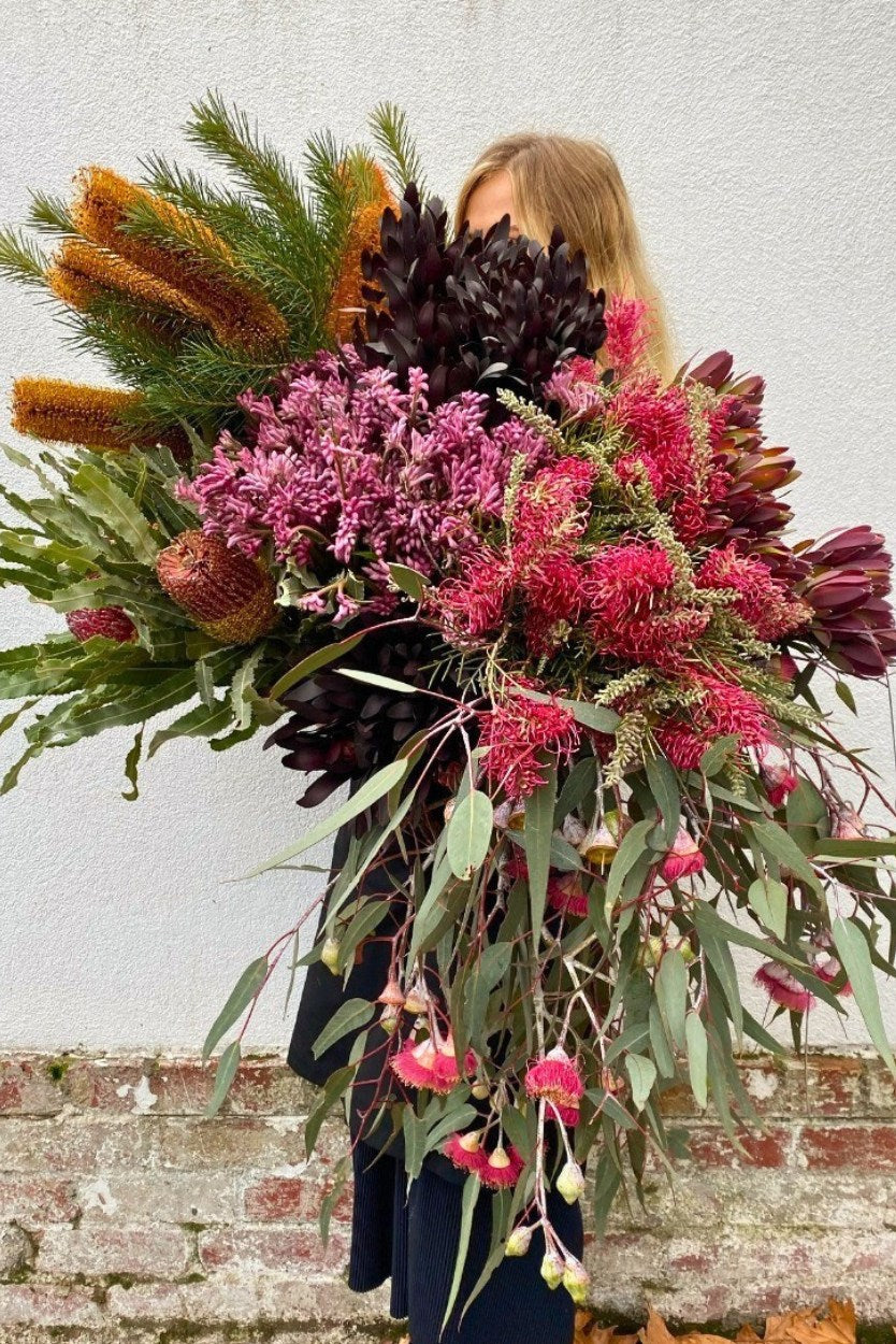 Person holding a large, colourful bouquet of native flowers against a light grey wall.