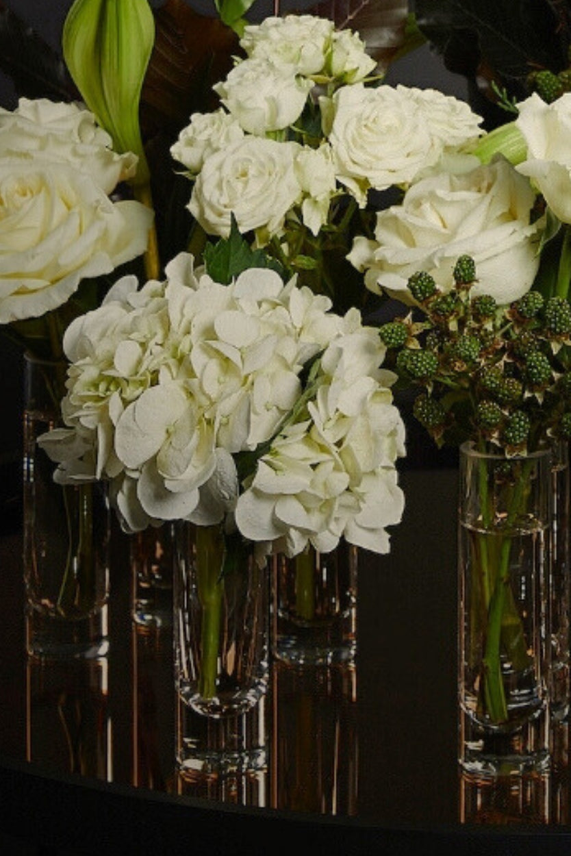 Bouquets of white flowers in clear vases on a reflective surface