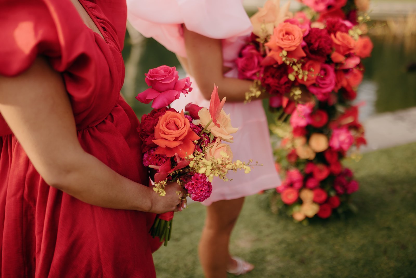 Person in a red dress holding a bouquet of flowers with another person in a pink dress in the background.