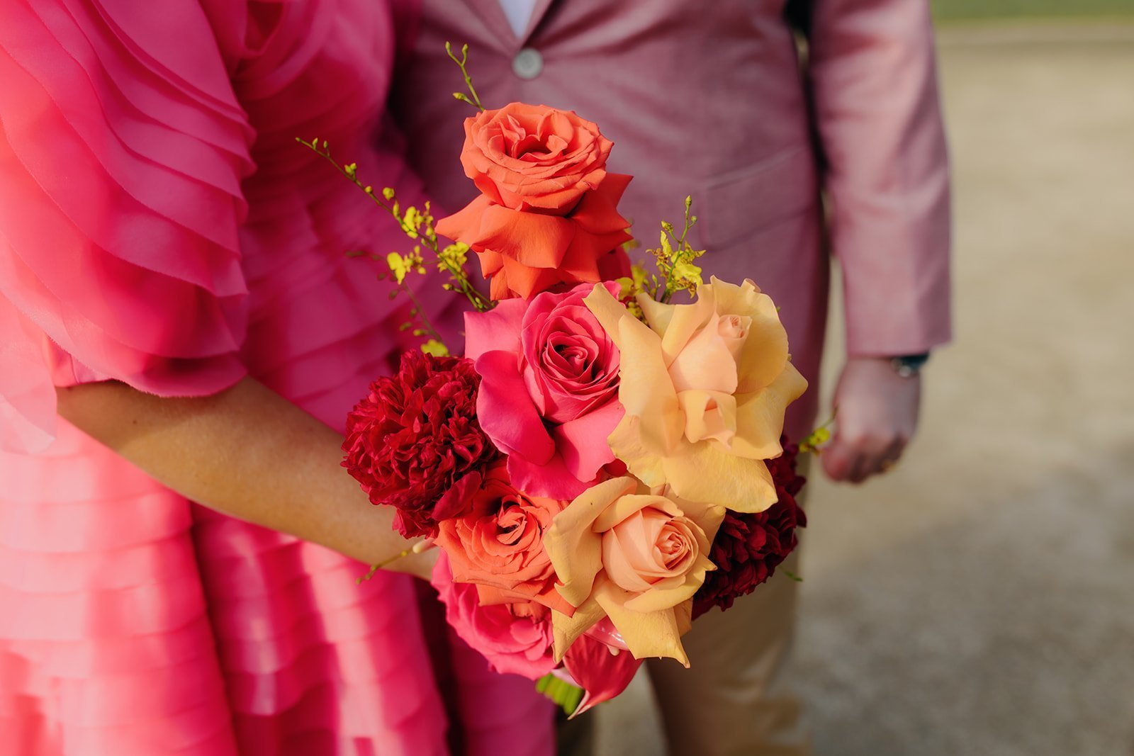 bridesmaid holding a bouquet of red, pink, and yellow flowers with a blurred background