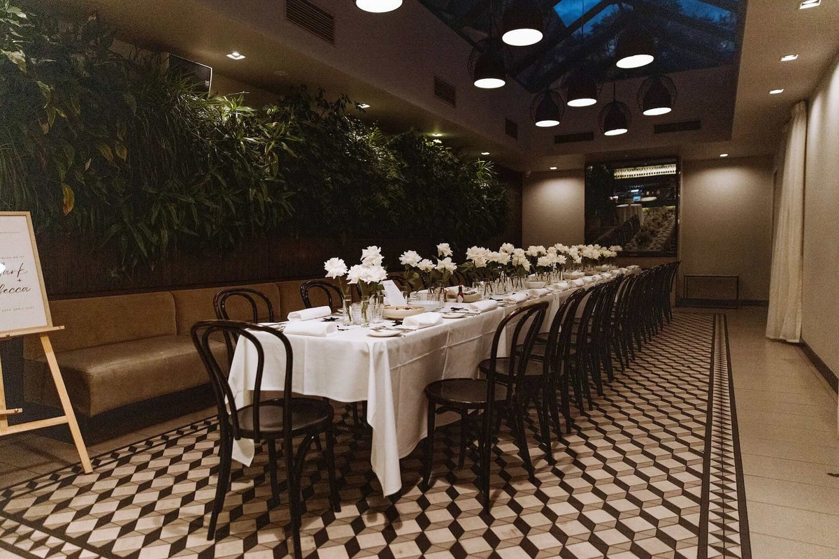 Dining setup with long table, chairs, and floral arrangements in a stylish room.