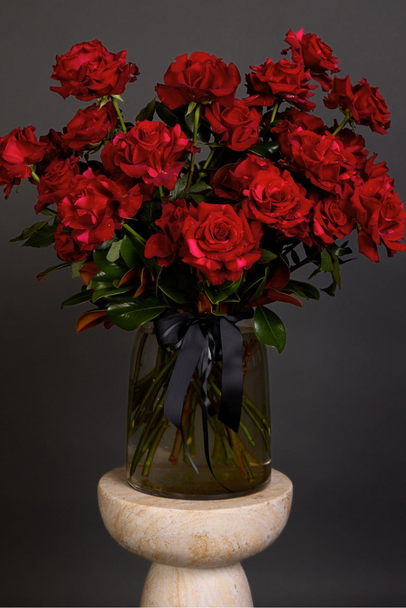 Bouquet of red roses in a clear vase with a black ribbon on a dark background