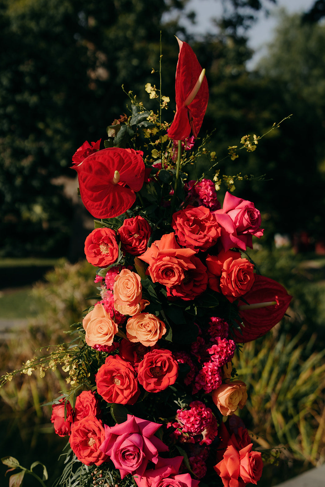 wedding flower arrangement of red, pink, and orange flowers with greenery against a blurred natural background