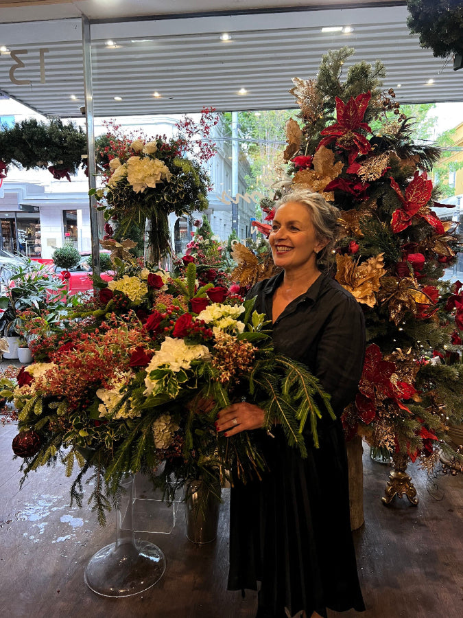 Woman holding a large floral arrangement in a store with Christmas decorations.