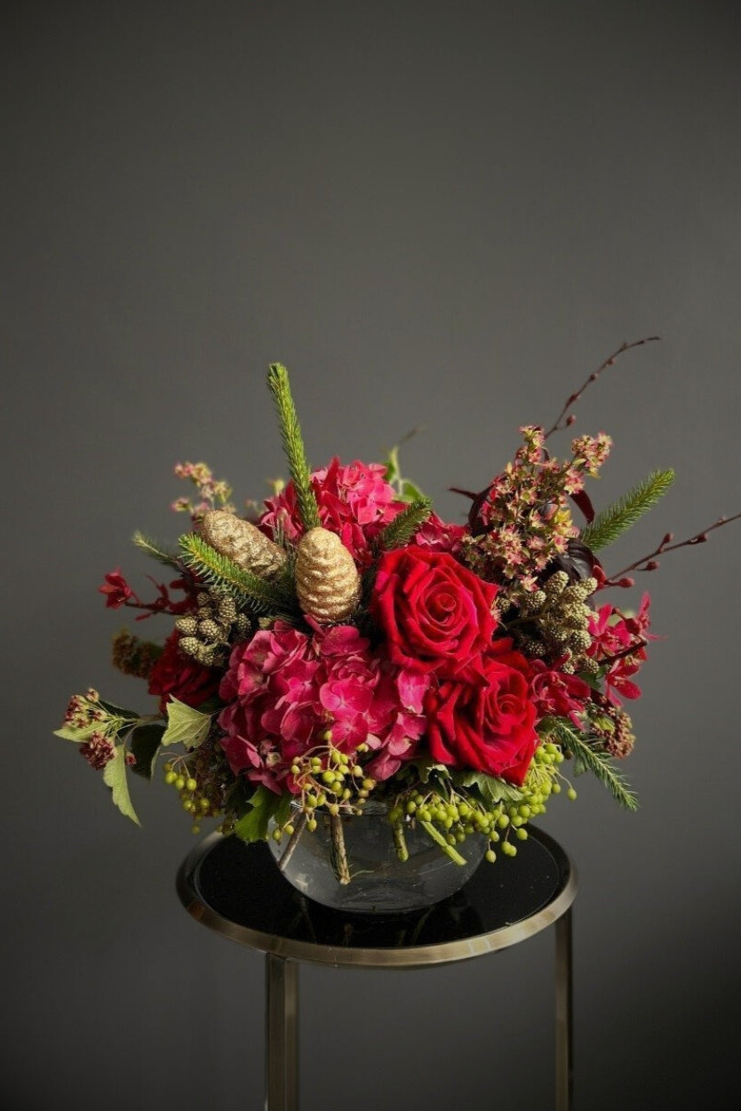 Christmas posy brimming with a selection of red summer blooms, berries, and festive foliages.