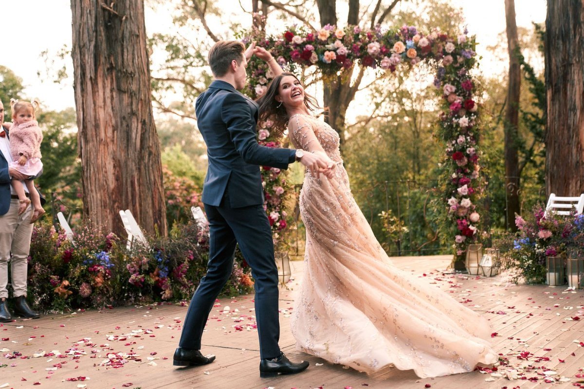 Man and woman dancing outdoors with a floral arch and decorations for their wedding