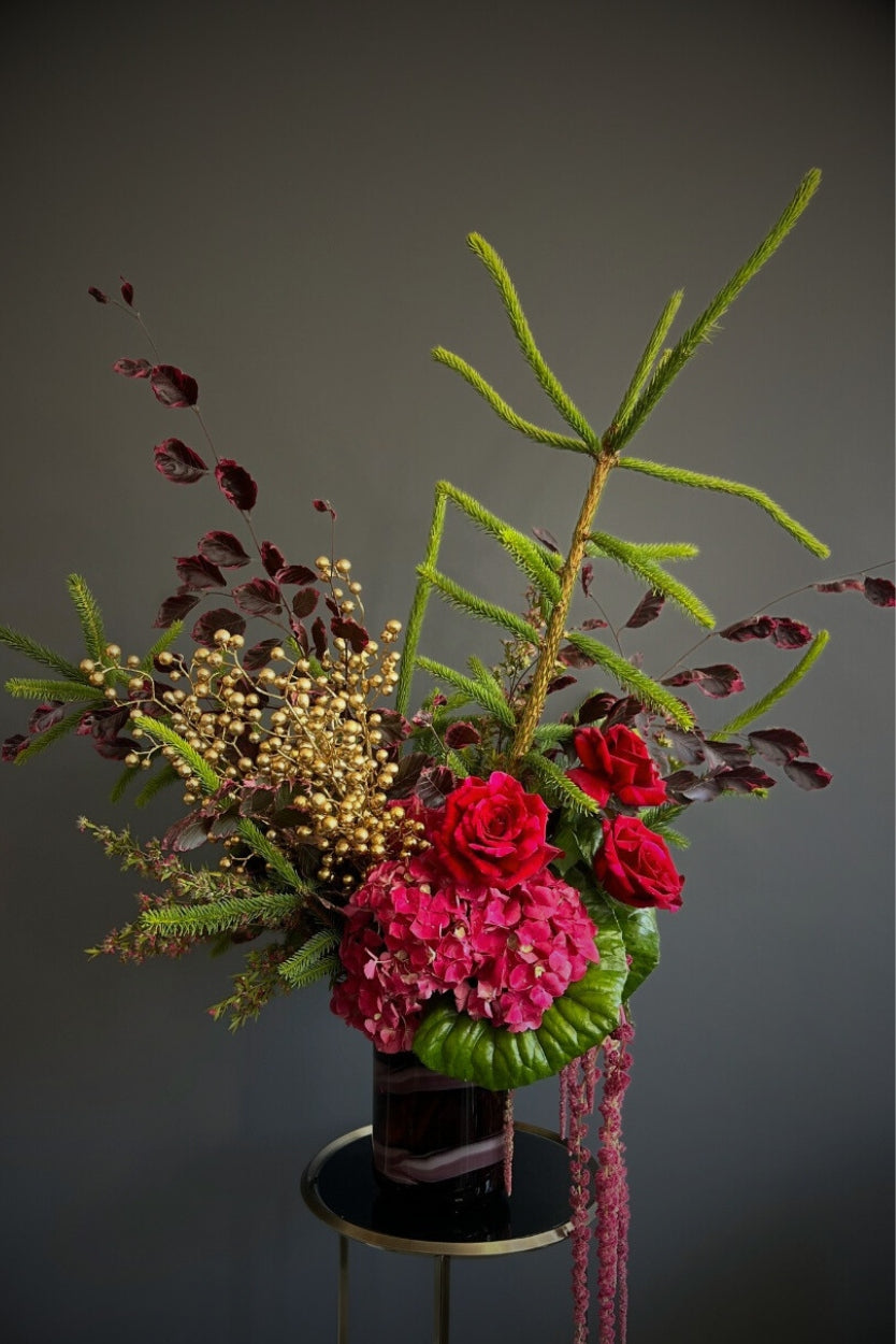 Floral arrangement with red and pink flowers and greenery on a dark background