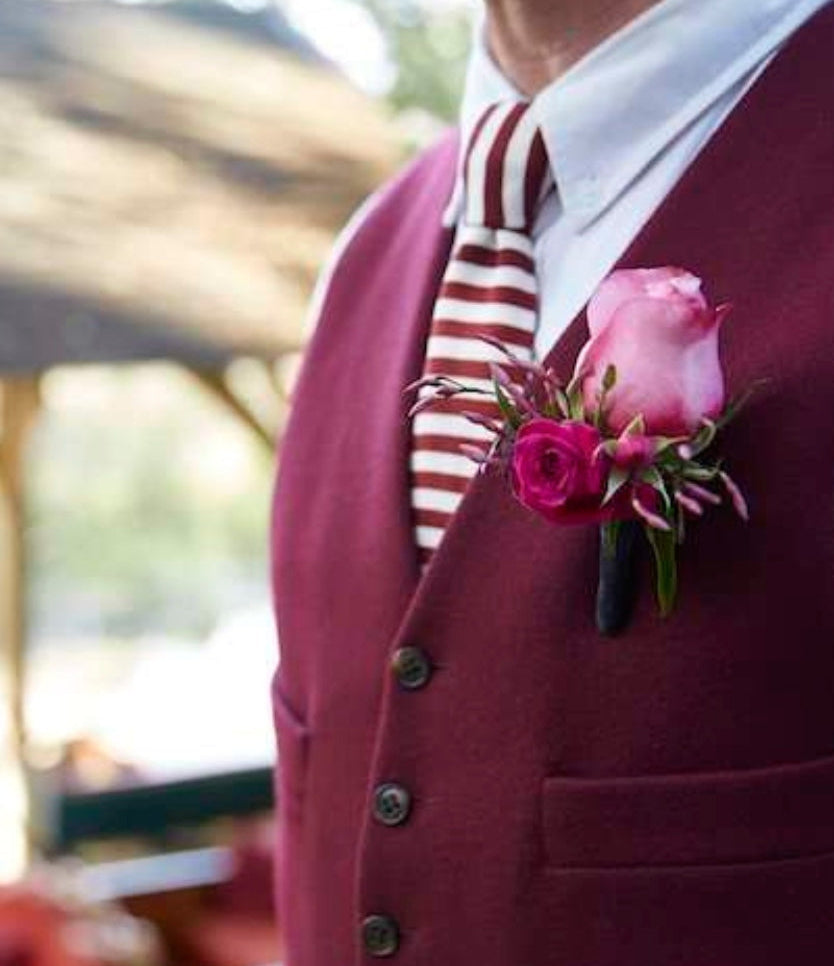 Man wearing a burgundy vest with a pink flower boutonniere and striped tie.