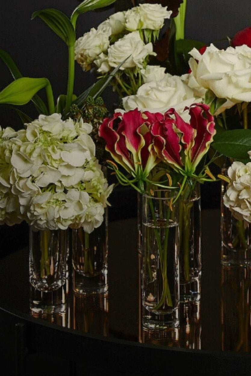 bud vases with festive flowers on a reflective surface against a dark background
